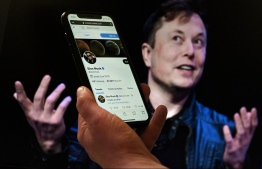 In this photo illustration, a phone screen displays the Twitter account of Elon Musk with a photo of him shown in the background, on April 14, 2022, in Washington, DC. - Tesla chief Elon Musk has launched a hostile takeover bid for Twitter, insisting it was a "best and final offer" and that he was the only person capable of unlocking the full potential of the platform. -- Photo: Olivier Douliery / AFP