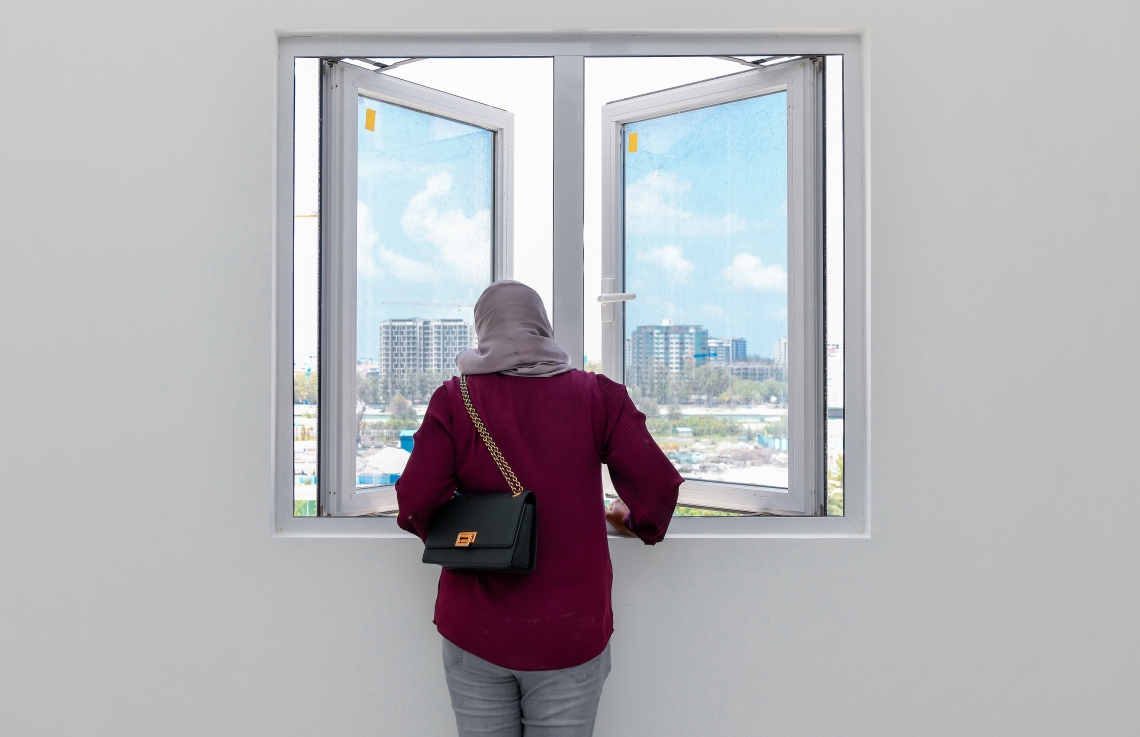 ސްޓެލްކޯގެ ފްލެޓަކަށް ދިރިއުޅުން ބަދަލުކުރަން ނިންމާފައިވާ ޒުވާން އަންހެނަކު، ފްލެޓެއްގެ ކުޑަދޮރުން ބޭރު ބަލައިލަނީ: މި ޒުވާނާގެ ދިރިއުޅުމަށް ވެސް މި އެޕާޓްމަންޓްތަކާއެކު ބޮޑު ކުރިއެރުމެއް އަންނާނެ ކަމަށް ބުނޭ.---ފޮޓޯ: ފަޔާޒު މޫސާ| މިހާރު