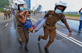 Policemen carry an injured man during a clash between government supporters and demonstrators outside the President's office in Colombo on May 9, 2022. - Police imposed an indefinite curfew in Sri Lanka's capital on May 9 after government supporters clashed with demonstrators demanding the resignation of President Gotabaya Rajapaksa. (Photo by Ishara S. KODIKARA / AFP)