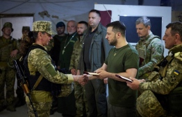 This handout picture taken and released by the press service of the Ukrainian Presidency on 18 June, 2022 shows Ukrainian President Volodymyr Zelensky (3rdR) awarding a servicewoman during his visit to the position of Ukrainian troops in Mykolaiv region. -- Photo by Handout / Ukraine Presidency/ AFP