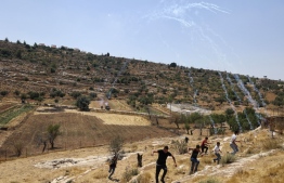 Palestinian demonstrators move away from Israeli tear gas while protesting attempts by Israeli settlers from the settlement of Eli to reportedly take control of a water spring in the village of Qaryut, south of Nablus in the occupied West Bank, on June 24, 2022. -- Photo: Jaafar Ashtiyeh / AFP