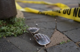 Police crime tape is seen near an American flag-themed sunglasses laying on the ground at the scene of the Fourth of July parade shooting in Highland Park, Illinois on July 4, 2022. - A shooter opened fire Monday during a parade to mark US Independence Day in the state of Illinois, killing at least six people, officials said. -- Photo: Youngrae Kim / AFP