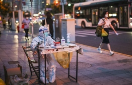 A health worker waits to test people for the Covid-19 coronavirus on a street next to a residential area in the Jing'an district of Shanghai on July 5, 2022. -- Photo: Hector Retamal / AFP