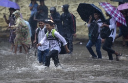 School children wade through a flooded street during rain showers in Mumbai on July 5, 2022. (Photo by Punit PARANJPE / AFP)