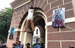 Activists stand under an effigy of Sri Lanka's President Gotabaya Rajapaksa, hanging from a clock tower near his official residence, in Colombo on July 10, 2022. - Sri Lankan protesters refused to budge from President Gotabaya Rajapaksa's residence on July 10, a day after they stormed his home, forcing him to flee with the navy and announce he would resign. -- Photo: Amal Jayasinghe / AFP