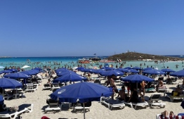 Beachgoers relax at Nissi Beach in the Cypriot resort town of Ayia Napa, one of the Mediterranean island's top tourist destinations, on July 17, 2022. - Beside sparkling Mediterranean waters at the Cypriot resort town of Ayia Napa, the bars are bouncing with foam dance parties as tourist numbers rebound following two tough years of pandemic. But one key nationality is effectively missing: Russian visitors, as the once lucrative market has been hit by European Union sanctions imposed after Moscow invaded Ukraine. -- Photo: Etienne Torbey / AFP