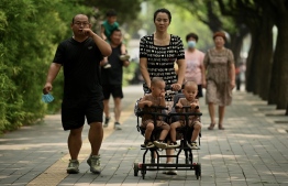 A woman pushes a trolley with twins along a street in Beijing on August 2, 2022. - China's population will begin to shrink by 2025, officials said, as family sizes grow smaller and citizens age. -- Photo: Noel Celis / AFP