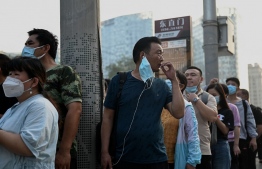 A man smokes a cigarette as he stands in a queue to catch a bus along a street in Beijing on August 1, 2022. -- Photo: Noel Celis / AFP
