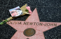 Flowers and a photo are placed on the star of Australian singer and actress Olivia Newton-John on the Hollywood Walk of Fame in Hollywood, California, on August 8, 2022. - Australian singer Olivia Newton-John, who gained worldwide fame as high-school sweetheart Sandy in the hit musical movie "Grease," died on August 8, 2022, her family said. She was 73. The entertainer, whose career spanned more than five decades, devoted much of her time and celebrity to charities after being diagnosed with breast cancer in 1992. -- Photo: Robyn Beck / AFP