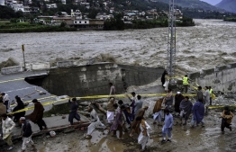 People gather in front of a road damaged by flood waters following heavy monsoon rains in Madian area in Pakistan's northern Swat Valley on August 27, 2022. - Thousands of people living near flood-swollen rivers in Pakistan's north were ordered to evacuate on August 27 as the death toll from devastating monsoon rains neared 1,000 with no end in sight. -- Photo: Abdul Majeed / AFP