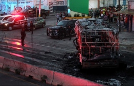 (FILES) In this file photo taken on August 9, 2022, members of the State Prosecutor's Office and Municipal Police guard the area where gang members set a bus on fire blocking a highway to prevent authorities from chasing them while they were clashing with another gang, in Zapopan, Jalisco State, Mexico. - Civilians killed, businesses set on fire and cities under siege -- escalating violence involving Mexican drug cartels has increased scrutiny of President Andres Manuel Lopez Obrador's "hugs not bullets" security strategy. Growing concerns that the approach is failing to stem the bloodshed come as Lopez Obrador's critics accuse him of trying to militarize the country by putting the National Guard under army control. (Photo by ULISES RUIZ / AFP)