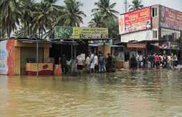 People gather in front of shops along a waterlogged street after heavy rains in a Bangalore on September 6, 2022. - Floods blamed on shoddy infrastructure crippled Indian IT hub Bangalore on September 5, with employees in the huge tech sector told to work from home and dozens of areas reportedly left without drinking water. (Photo by Manjunath Kiran / AFP)