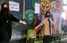 This image grab taken from a UGC video posted on October 19, 2022 shows two women, who are not observing Iranian headscarf laws, standing while giving hugs to passersby on a street in the Ekbatan Town in Tehran. A sign on the wall behind the women reads: "Hugs for those who are sorrowful". - Iran has been rocked by weeks of protests since 22-year-old Masha Amini's death was announced on September 16, three days after she was arrested by morality police in Tehran for allegedly violating the country's strict dress code for women. -- Photo by various sources / AFP