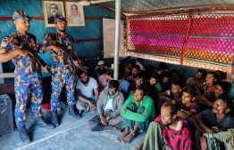 This handout photograph taken on October 28, 2022, and released by Bangladesh Armed Police Battalion (APBN) shows detained Rohingya refugees sit next to security personal after crackdown in Rohingya refugee camp in Ukhia 28, 2022. - Myanmar had detained 80 Rohingya people seeking to flee the nation via boat -- Photo by Bangladesh Armed Police Battalion (APBN) / AFP