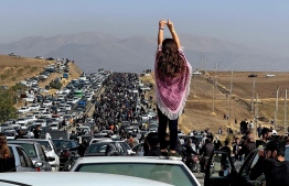 This UGC image posted on Twitter reportedly on October 26, 2022 shows an unveiled woman standing on top of a vehicle as thousands make their way towards Aichi cemetery in Saqez, Mahsa Amini's home town in the western Iranian province of Kurdistan, to mark 40 days since her death, defying heightened security measures as part of a bloody crackdown on women-led protests. - A wave of unrest has rocked Iran since 22-year-old Amini died on September 16 following her arrest by the morality police in Tehran for allegedly breaching the country's strict rules on hijab headscarves and modest clothing. -- Photo: UGC / AFP