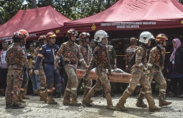 Fire and rescue department workers carry out the body of a victim after a landslide in Batang Kali, Selangor on December 16, 2022. - At least 16 people were killed when a landslide struck a campsite at a Malaysian farm on December 16, 2022, officials said, with rescuers scouring the muddy terrain for nearly 20 people still missing. -- Photo: Arif Kartono / AFP