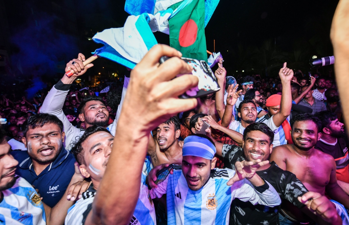 ވޯލްޑް ކަޕްގެ ފައިނަލް މެޗު ބަލަން އާޓިފިޝަލް ބީޗް ސަރަހައްދަށް ޖަމާވި އާޖެންޓީނާ އަށް ސްޕޯޓުކުރާ ބަންގްލަދޭޝްގެ ބަޔަކު ފޯނުން ގްރޫޕް ފޮޓޯއެއް ނަގަން ތައްޔާރުވަނީ.--- ފޮޓޯ: ފަޔާޒު މޫސާ | މިހާރު