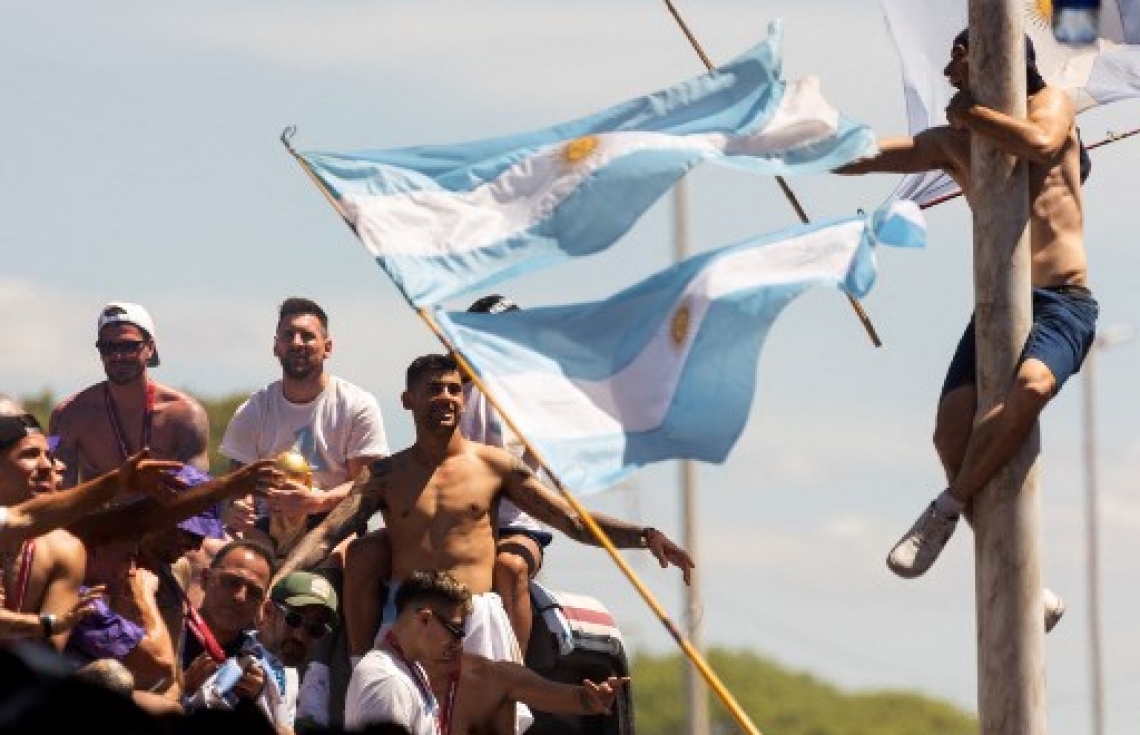 ވޯލްޑް ކަޕުގެ ތަށި ހިފައިގެން އާޖެންޓީނާ ކުޅުންތެރިން އެ ގައުމުގެ ވެރިރަށް ބީނޯސް އޭރީޒްގައި ބޭއްވި ބަސް ޕެރޭޑުގައި އާންމުންގެ މީހަކު އެތާހުރި ހޮޅިދަނޑި މައްޗަށް އަރައިގެން، ޓީމުގެ ކުޅުންތެރިންނަށް މަރުހަބާ ކިޔަނީ: މިއީ އާޖެންޓީނާ ވޯލްޑް ކަޕް ތަށި އުފުލާލި ތިންވަނަ ފަހަރު.-- ފޮޓޯ: އޭއެފްޕީ