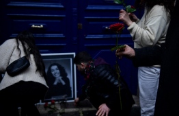 Protesters lay roses in front of a portrait of the La Fayette street murders victims in Paris in 2013, as they take part in a demonstration to pay tribute to them and to those of the recent Enghien Street shooting on December 23, 2022, during a march in solidarity with the Kurdish community in Paris on December 26, 2022. -- Photo: Julien De Rosa / AFP