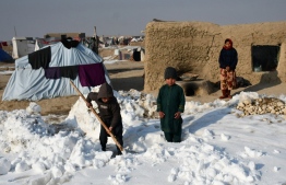 Afghan internally-displaced children shovel snow near their tents during a cold winter day at Nahr-e Shah-e- district of Balkh Province, near Mazar-i-Sharif on January 17, 2023. - At least 70 people have died in a wave of freezing temperatures sweeping Afghanistan, officials said on Janaury 18, as extreme weather compounds a humanitarian crisis in the poverty-stricken nation. -- Photo: Atif Aryan / AFP