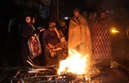 People warm themselves around a bonfire in the rubble in Kahramanmaras, Turkey, after a 7.8-magnitude earthquake struck the country's southeast on February 7, 2023. - A major 7.8-magnitude earthquake struck Turkey and Syria, killing more than 3,000 people and flattening thousands of buildings as rescuers dug with bare hands for survivors. -- Photo: Adem Altan / AFP