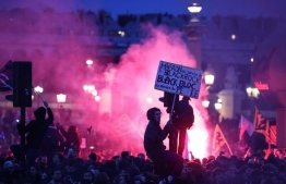 A protester on a traffic light holds a placard reading "Macron at the service of Black Rock, Black bloc at the service of the people" during a demonstration on Place de la Concorde after the French government pushed a pensions reform through parliament without a vote, using the article 49,3 of the constitution, in Paris on March 16, 2023. - The French president on March 16 rammed a controversial pension reform through parliament without a vote, deploying a rarely used constitutional power that risks inflaming protests. The move was an admission that his government lacked a majority in the National Assembly to pass the legislation to raise the retirement age from 62 to 64. -- Photo: Thomas Samson / AFP
