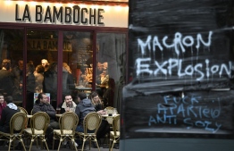 Costumers sit on a terrace next to a hand-written message reading "Macron Explosion", on the day of a ruling from France's Constitutional Council on a contested pension reform pushed by the French government, in Rennes, western France, on April 14, 2023. - France's top constitutional court is to rule on April 14 on whether to approve the French President's deeply unpopular pensions overhaul after months of protests. -- Photo: Damien Meyer / AFP