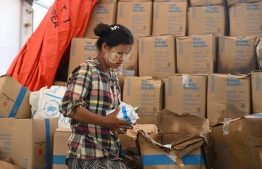 A woman sorts out food at a damaged UN World Food Programme warehouse in Sittwe on May 17, 2023, in the aftermath of Cyclone Mocha's landfall. The death toll in cyclone-hit Myanmar rose to at least 81, according to local leaders, officials and state media, as villagers tried to piece together ruined homes and waited for aid and support. -- Photo: Sai Aung Main / AFP