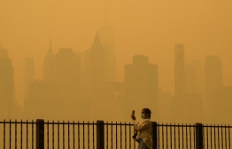A person wearing a face mask takes photos of the skyline as smoke from wildfires in Canada cause hazy conditions in New York City on June 7, 2023. An orange-tinged smog caused by Canada's wildfires shrouded New York on Wednesday, obscuring its famous skyscrapers and causing residents to don face masks, as cities along the US East Coast issued air quality alerts. -- Photo: Angela Weiss / AFP