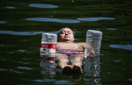 A man uses water bottles for flotation as he cools off in a canal in Beijing on June 22, 2023. Swathes of northern China sweltered in 40-degree heat on June 22, weather data showed, as parts of Beijing and the nearby megacity of Tianjin recorded their highest temperatures for years. -- Photo: Greg Baker / AFP