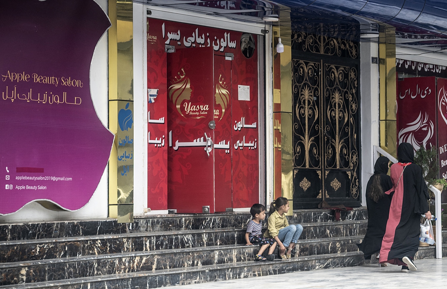 ކާބުލްގެ ބިއުޓީ ޝޮޕެއް ކުރިމަތީގައި ކުޑަ ދެ ކުއްޖަކު އިއްޔެ އިށީނދެލައިގެން: އަފްގާނިސްތާނުގައި ސެލޫންތައް ބަންދުކުރަން ވަނީ ނިންމައިފައި -- ފޮޓޯ: އޭއެފްޕީ