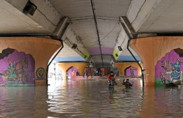 A family wades through the flood under a bridge after Yamuna River overflowed due to heavy monsoon rains in New Delhi on July 14, 2023. Days of relentless monsoon rains have killed at least 66 people in India, government officials said on July 12, with dozens of foreign tourists stranded in the Himalayas after floods severed road connections. (Photo by Arun SANKAR / AFP)