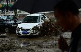 A man walks past a car damaged after the Yongding river breached its banks, after heavy rains in Mentougou district in Beijing on August 1, 2023. At least 11 people are dead and 27 missing after heavy rains lashed Beijing, state media said on August 1, in downpours that have submerged roads and deluged neighbourhoods with mud. -- Photo: Pedro Pardo / AFP