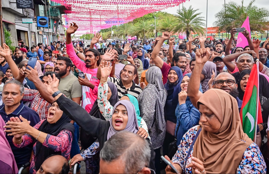 ކުރީގެ ރައީސް ޔާމީން ޖަލުން ގޭ ބަންދަށް ބަދަލުކުރުމުން އެ މަނިކުފާނު ގެކޮޅުގެ ކުޑަދޮރުން ސަޕޯޓަރުންނަށް ވޭވް ކުރައްވާއިރު އެ މީހުން އުފަލުން އެކަން ބަލައިގަންނަނީ: ޔާމީނަށް މަރުހަބާ ކިޔަން އެތައް ސަތޭކަ ބަޔަކު އެ މަނިކުފާނުގެ ގެކޮޅު ކައިރި އަށް ޖަމާވި. ޔާމީނަށް އިސްވެ މަރުހަބާ ދެންނެވީ އިންތިހާބީ ރައީސް ޑރ. މުހައްމަދު މުއިއްޒު.---ފޮޓޯ: ނިޝާން އަލީ| މިހާރު