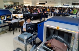 This photo taken on October 4, 2023 shows departing travellers (background) waiting in line for security checks as officials screen carry-on luggage at the Ninoy Aquino International Airport in metro Manila. Security patrols and sniffer dogs were deployed at dozens of Philippine airports on October 6, after the aviation regulator received a bomb threat against commercial planes. -- Photo: AFP
