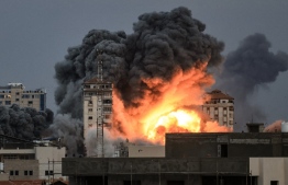 EDITORS NOTE:  / People standing on a rooftop watch as a ball of fire and smoke rises above a building in Gaza City on October 7, 2023 during an Israeli air strike that hit the Palestine Tower building. At least 70 people were reported killed in Israel, while Gaza authorities released a death toll of 198 in the bloodiest escalation in the wider conflict since May 2021, with hundreds more wounded on both sides. (Photo by MAHMUD HAMS / AFP)