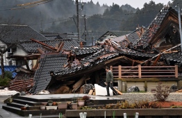 A man walks past a collapsed house in Anamizu Town, Ishikawa prefecture on January 3, 2024, after a major 7.5 magnitude earthquake struck the Noto region in Ishikawa prefecture on New Year's Day. Japanese rescuers scrambled to search for survivors on January 3 as authorities warned of landslides from heavy rain after a powerful earthquake that killed at least 62 people. -- Photo: Kazuhiro Nogi / AFP