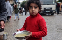A displaced Palestinian child carries a ration of red lentil soup, distributed by volunteers in Rafah in the southern Gaza Strip on February 18, 2024, amid the ongoing conflict between Israel and the militant group Hamas. After more than four months of war that has flattened huge swathes of the Strip, Gazans are inching closer towards famine, according to the UN's World Food Programme. (Photo by SAID KHATIB / AFP)