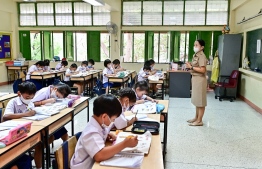 This photo taken on January 22, 2024 shows pupils wearing face masks inside a classroom with open windows at Suanlumpinee School in Bangkok. Hundreds of Thai children strain to sing the national anthem, reedy voices and fragile lungs competing against eight lanes of belching traffic next to their school's open atrium in central Bangkok. -- Photo: Manan Vatsyayana / AFP