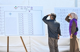 A voter and an election official observing the board placed outside the voter tent detailing location and numbers of various ballots boxes. -- Photo: Fayaz Moosa / Mihaaru News