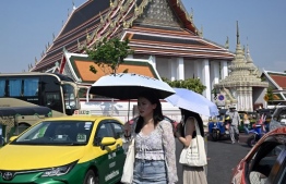 (FILES) Tourists shield themselves from the sun with umbrellas to combat the heat outside Wat Pho Buddhist temple in Bangkok on April 1, 2024. Thai authorities issued an extreme heat warning for Bangkok on April 24, 2024 urging people to stay indoors for their own safety as temperatures soared. (Photo by Lillian SUWANRUMPHA / AFP)