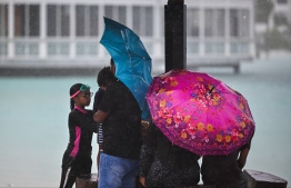 A group of people at Rasfannu Beach as it rains heavily. Stormy weather is predicted for the rest of the week.-- Photo: Fayaz Moosa / Mihaaru