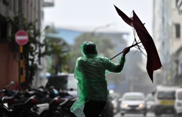 Man walking on Majeedhee Magu, struggling to hold on to his umbrella in strong winds.-- Photo: Fayaz Moosa / Mihaaru