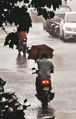 Motorist trying to find shelter from the rain and winds with an umbrella.-- Photo: Nishan Ali / Mihaaru