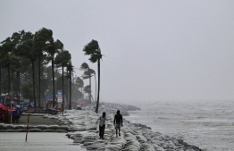 People walk along a beach during rainfall following the landfall of Cyclone Remal in Kuakata on May 27, 2024. Residents of low-lying coastal areas of Bangladesh and India surveyed the damage on May 27 as an intense cyclone weakened into heavy storm, with at least two people dead, roofs ripped off and trees uprooted. -- Photo: Munir Uz Zaman / AFP