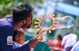 A child blowing bubbles with a parent at the Bubble Show held for children in Baa Kendhoo Volleyball Court to colorfully celebrate Eid-al-Adha festivities. -- Photo: Fayaz Moosa / Mihaaru News