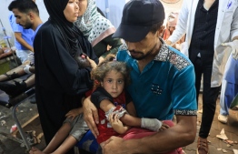 ހާލުގައި ޖެހިފައިވާ މީހުން ހިޔާމަތް ހޯދާ ސްކޫލަށް އިޒްރޭލުން އިއްޔެ ދިން ހަމަލާގައި ޒަހަމްވި ކުއްޖަކު ނަގައިގެން ގެންދަނީ. -- ފޮޓޯ: އޭއެފްޕީ