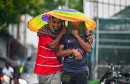 Two foreigners sharing an umbrella during heavy rain in Male' City yesterday. -- Photo: Fayaz Moosa / Mihaaru News