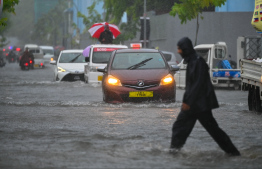 A man crossing a flooded road in Male' City as cars travel in the heavy rain. -- Photo: Fayaz Moosa / Mihaaru News