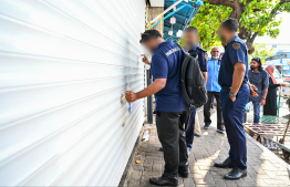 An Immigration officer attempting to open gates of a store that was quickly slid shut during yesterday's operations. -- Photo: Fayaz Moosa / Mihaaru News